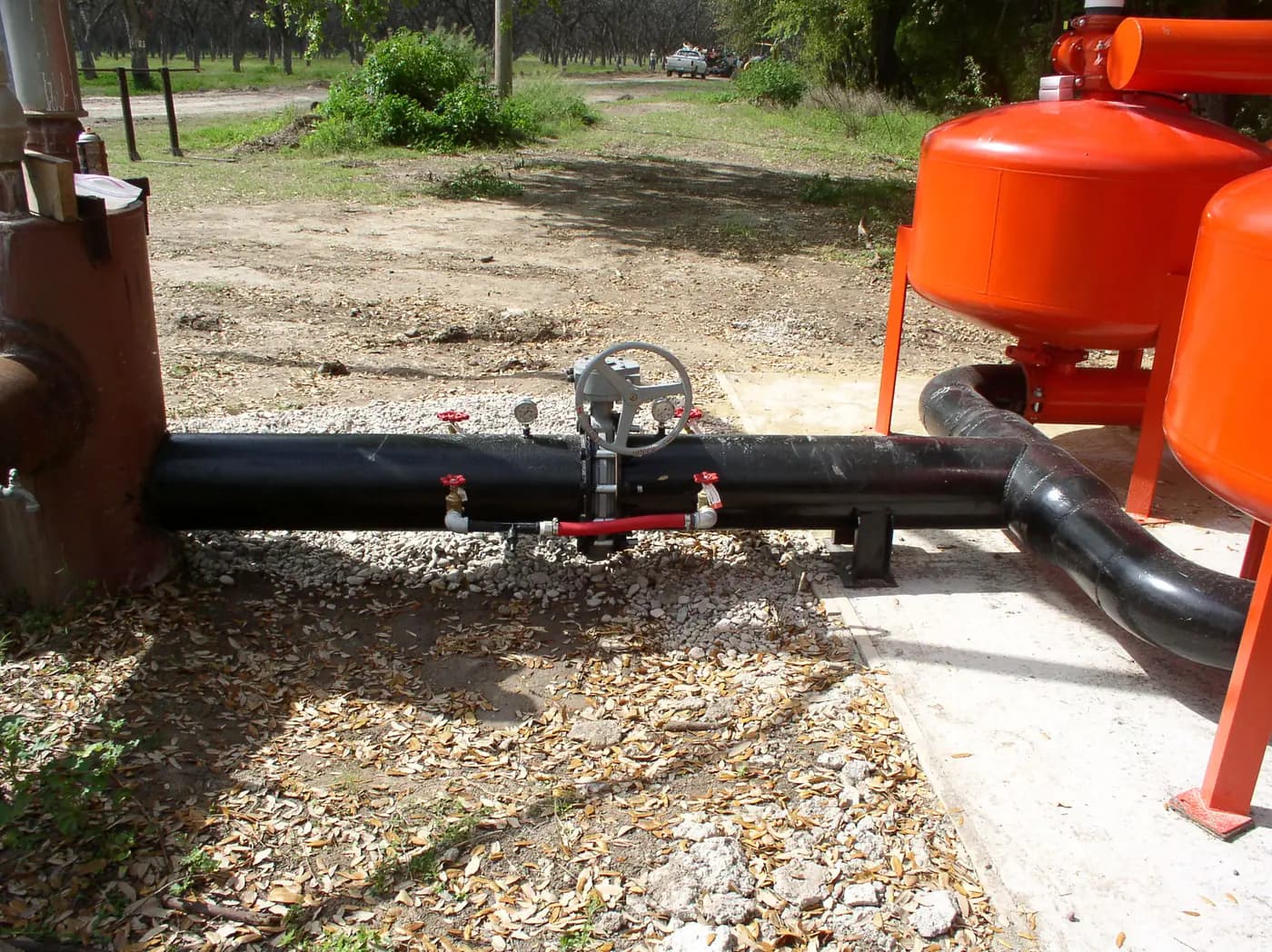 Irrigation control valves and pipework beside red filter tanks at a Texas pecan farm