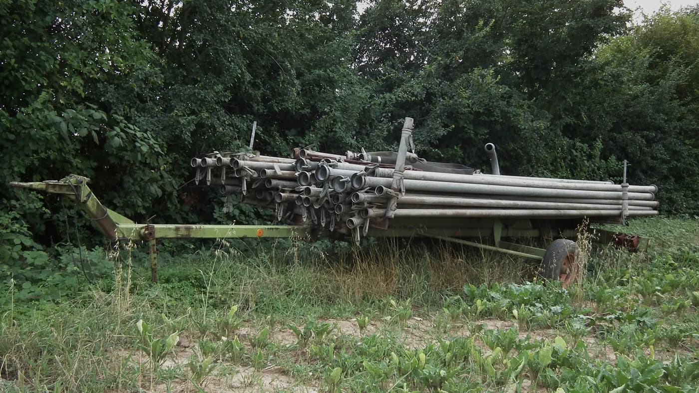 Detached metal irrigation pipes stacked on a trailer beside a field in Germany
