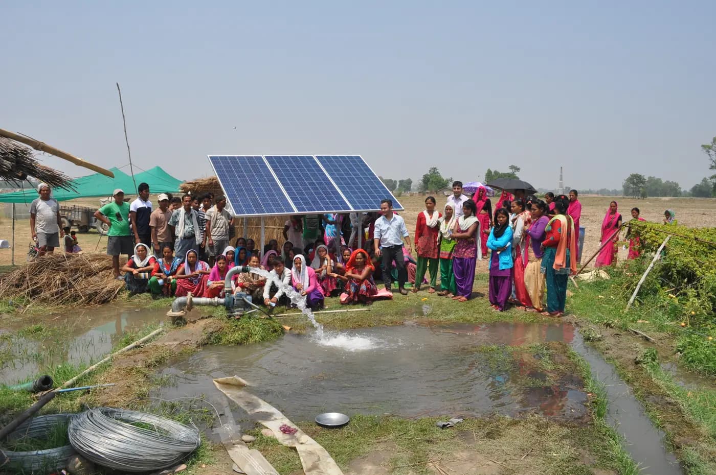 Personas junto a una bomba de agua solar que descarga agua cerca de tierras agrícolas en Nepal
