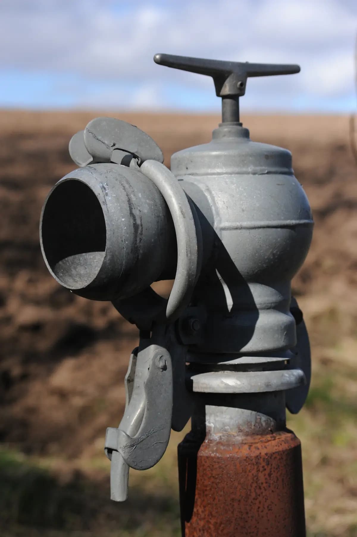 Weathered metal irrigation valve and open pipe connection in a cultivated field
