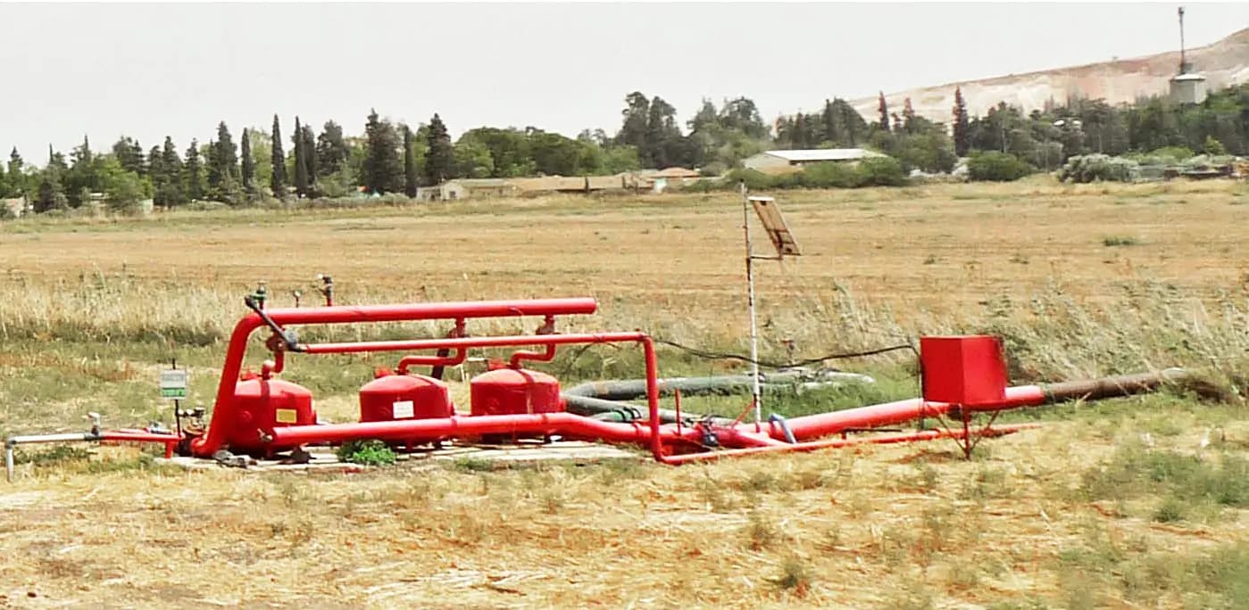 Bomba de riego y depósito conectados por tuberías junto a tierras agrícolas